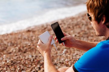 Mann på strand som lader smarttelefon med powerbank