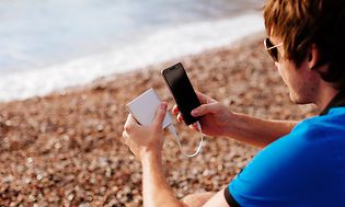 Mann på strand som lader smarttelefon med powerbank