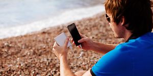Mann på strand som lader smarttelefon med powerbank