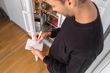 Mann noterer foran åpent kjøleskap