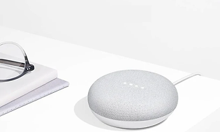 Hvit Google Home hub på et bord ved siden av et par briller