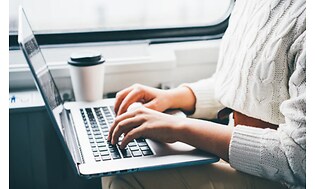 kvinne skriver på laptop på tog
