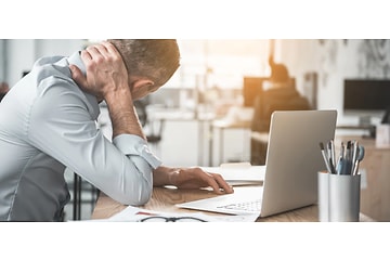 Mann masserer nakken pga smerter foran laptop på kontor