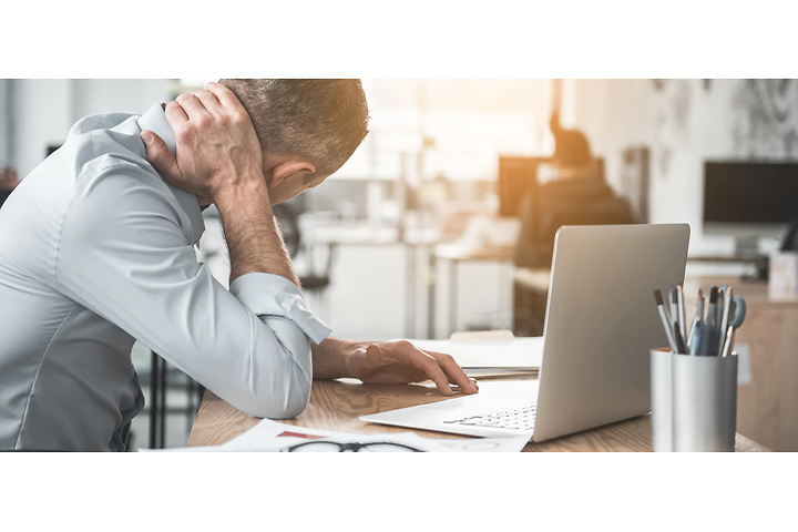 Mann masserer nakken pga smerter foran laptop på kontor