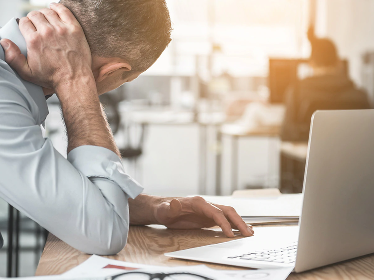 Mann masserer nakken pga smerter foran laptop på kontor