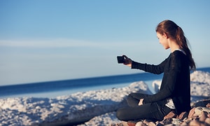en kvinne ser på smarttelefon mens hun sitter på en strand