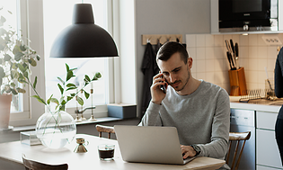 en mann jobber poå sin bærbare PC mens han snakker i smarttelefonen på et kjøkken