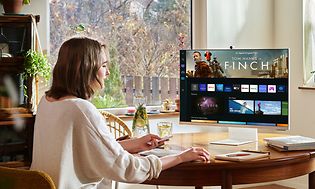 Kvinne som sitter ved spisebord og bruker en Samsung Smart Monitor