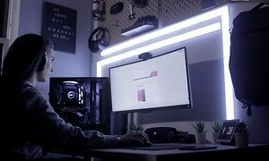 Kvinne med hodetelefoner sitter konsentrert foran PC med LIFX lysplankesett bak som lyser sterkt blåhvitt lys