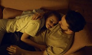 En mann og en kvinne klemmer hverandre i en sofa i et rom med mykt gult lys