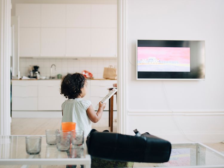 Liten jente holder fjernkontrollen foran en TV