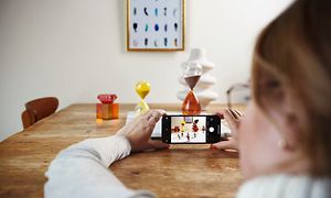 kvinne tar bilde av flere gjenstander på et bord med sin iPhone