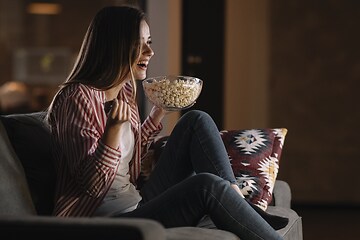 Jente ser på en film i TV-sofaen med popcorn