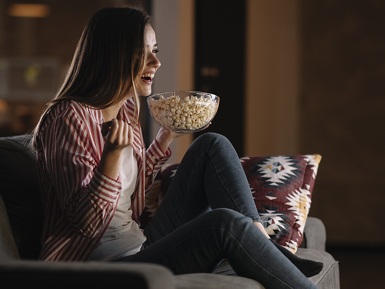 Jente ser på en film i TV-sofaen med popcorn