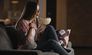 Jente ser på en film i TV-sofaen med popcorn