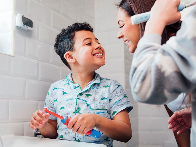 Familie på badet og en liten gutt som viser tennene til moren sin og holder en elektrisk tannbørste i hånden