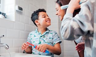 Familie på badet og en liten gutt som viser tennene til moren sin og holder en elektrisk tannbørste i hånden