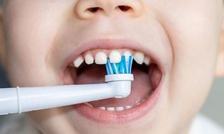 Nærbilde på en småbarns munn og et elektrisk tannbørstehode som pusser tennene