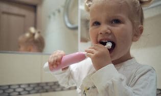 En glad liten jente på badet pusser tennene med en elektrisk tannbørste