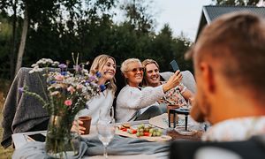 To jenter og en gutt tar en selfie i hagen mens de sitter rundt et bord.