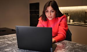 Kvinne sitter i et kjøkken foran en Lenovo Yoga Slim 7 Pro X bærbar PC