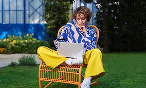 Kvinne sitter i hagen på en oransje stol med en Lenovo Yoga Slim 9 på fanget