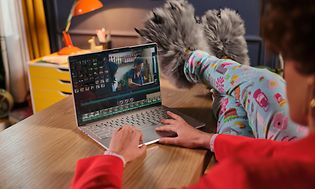 Kvinne redigerer video på en Lenovo Yoga Slim 9 med beina på bordet