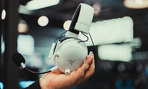 En hånd som holder opp et hvitt gamingheadset fra Razer
