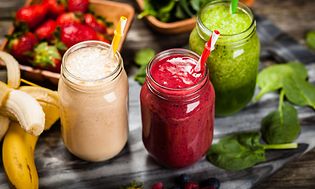 Tre glass med ulike smoothier med frukt og grønt liggende rundt