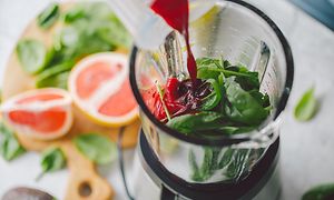 Innsiden av en blender med spinat og rød juice helles over