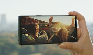 person holder Sony Xperia 1 IV sidelengs med bilde av to personer i en bil på skjermen