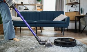 En person som bruker en trådløs støvsuger i en stue ved siden av en svart robotstøvsuger