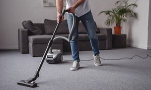 En mann støvsuger med en støvsuger med ledning i en grå stue