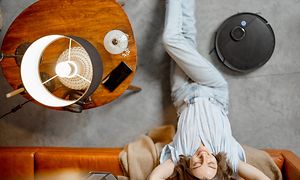 En kvinne slapper av i nærheten av en sofa og en robotstøvsuger på gulvet