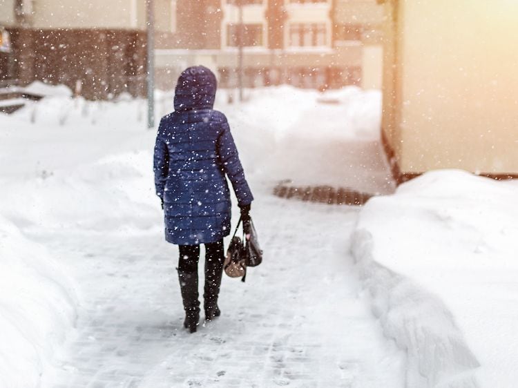 Kvinne sett bakfra som vandrer gjennom bygate i kraftig snøvær om vinteren