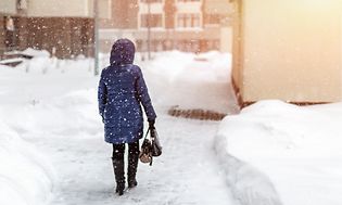 Kvinne sett bakfra som vandrer gjennom bygate i kraftig snøvær om vinteren