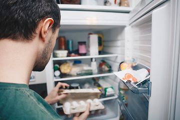 mann holder en åpen pakke med egg i et åpent kjøleskap
