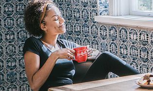 Kvinne som drikker fra kaffekopp med kaffemaskin på bordet