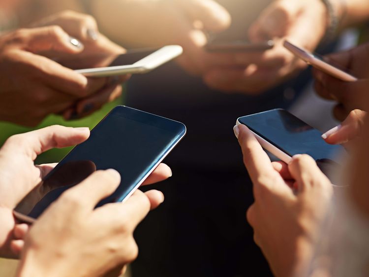 en gruppe personer står sammen og bruker smarttelefon utendørs