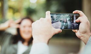 person holder smarttelefon og fotograferer smilende kvinne