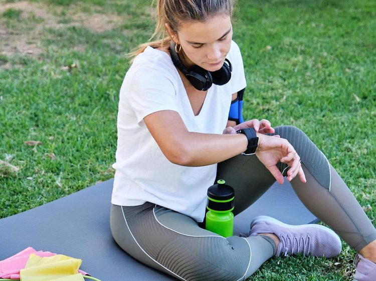 en kvinne sjekker smartklokken sin mens hun sitter utendørs på en yogamatte