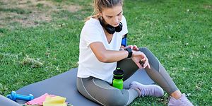 en kvinne sjekker smartklokken sin mens hun sitter utendørs på en yogamatte