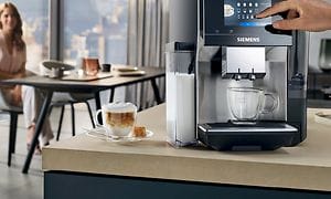 Siemens EQ700 på en kjøkkenbenk, en kopp kaffe og en kvinne i bakgrunnen