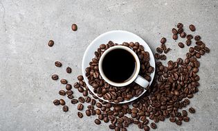 Kaffekopp med kaffebønner strødd rundt den på grått bord