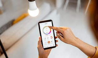 en kvinne justerer smartbelysning via app på smarttelefon