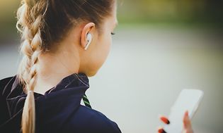 kvinne med ørepropper i ørene ser på smarttelefon