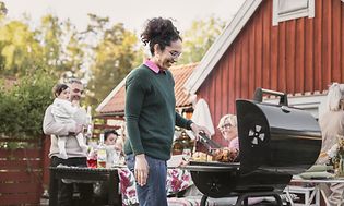 kvinne står og griller med mennesker i bakgrunnen