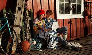 to tenåringer sitter utendørs og jobber på en MacBook Air
