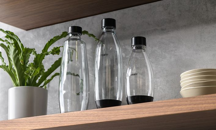 Tre Sodastream-flasker på ei hylle med en grønn plante