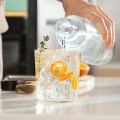 person heller boblefann fra en flaske over i et glass med frukt og isbiter